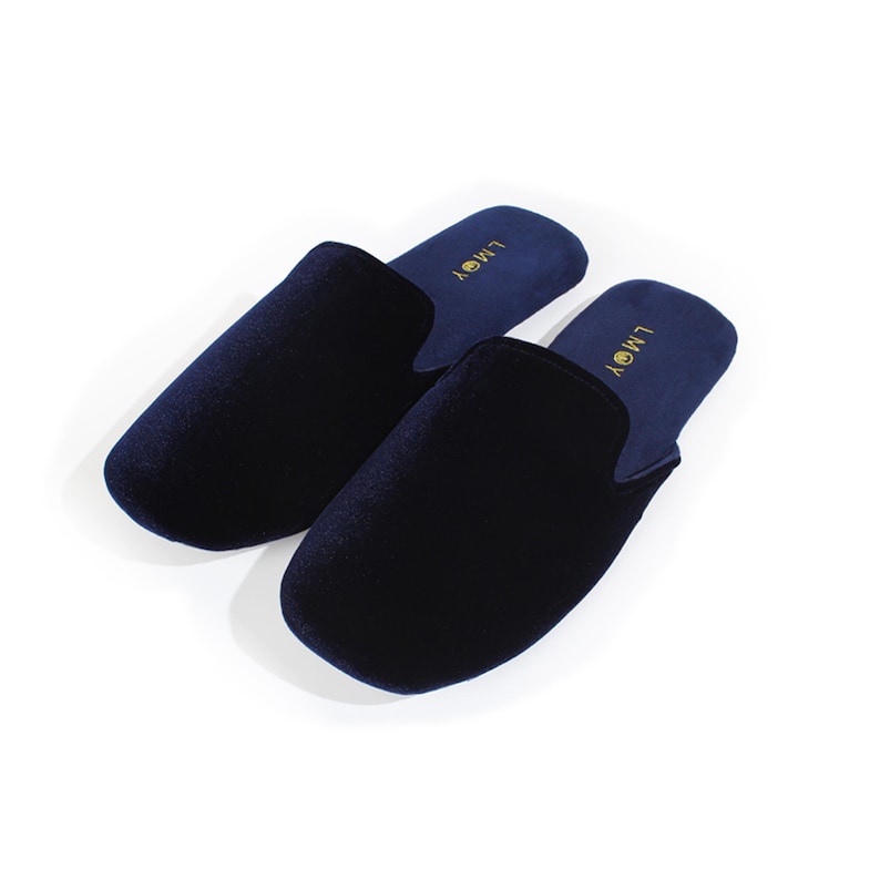 May include: A pair of dark navy blue velvet slippers with a rounded toe design. The interior footbed is lined in a matching navy blue fabric and features the gold-coloured text LMOY printed near the heel area of each slipper.