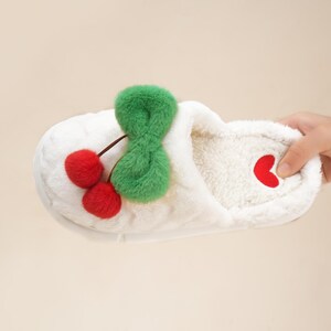 Pu&ograve; includere: Pantofola in peluche bianca con design a ciliegia. La pantofola presenta due pompon a ciliegia rossi con uno stelo verde e un accento a cuore rosso. L'interno &egrave; in morbido materiale bianco.