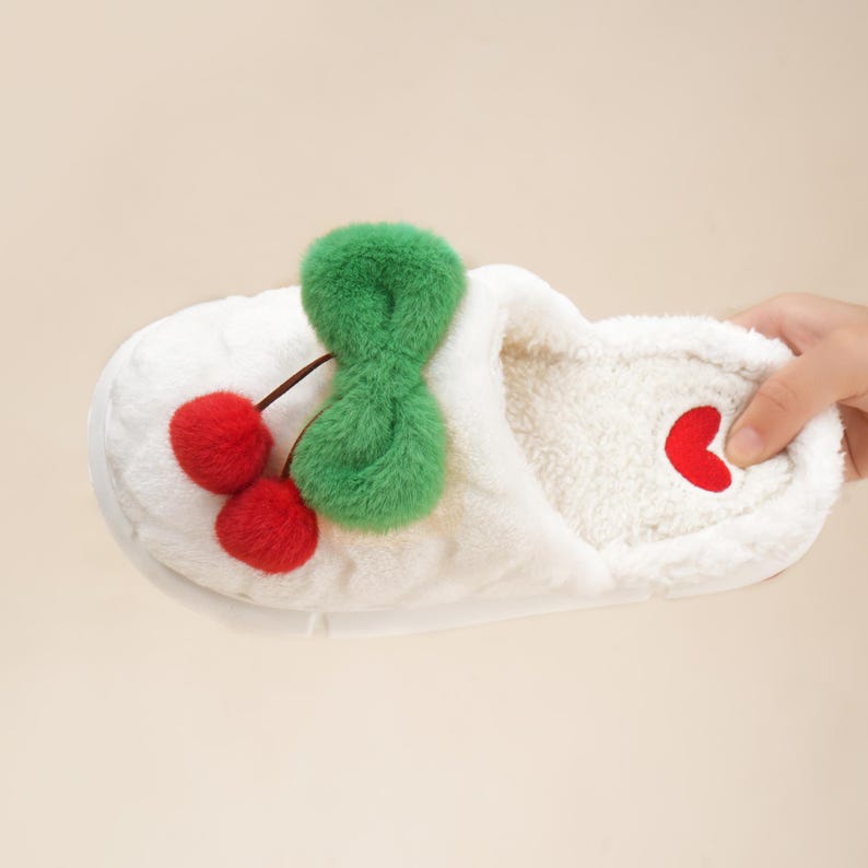 Pu&ograve; includere: Pantofola in peluche bianca con design a ciliegia. La pantofola presenta due pompon a ciliegia rossi con uno stelo verde e un accento a cuore rosso. L'interno &egrave; in morbido materiale bianco.