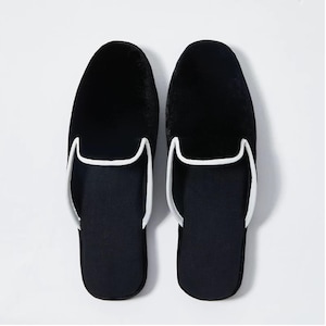 May include: A pair of black velvet slippers with white piping around the edges. The slippers have a closed toe and a slip-on design.