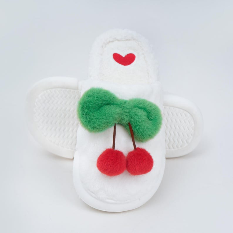 Pu&ograve; includere: Pantofole in peluche bianche con un fiocco verde e due ciliegie rosse. Un piccolo cuore rosso &egrave; sulla parte superiore della pantofola. Le pantofole hanno una suola strutturata.