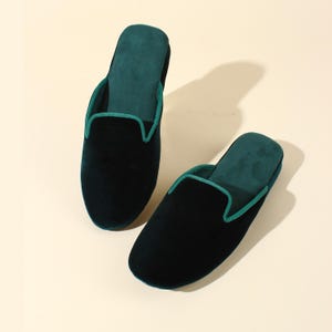 May include: A pair of dark green velvet slippers with a green trim. The slippers are made of a soft, comfortable material and have a slip-on design.