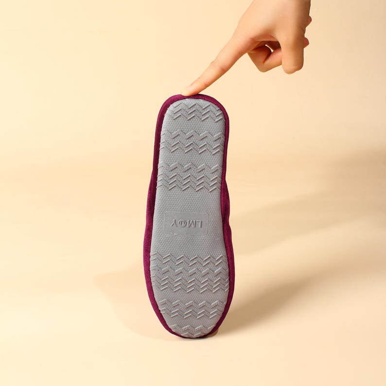 May include: The bottom of a burgundy slipper with a gray non-slip sole. The sole has the text "L'm@y" printed on it.