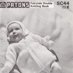 Puede incluir: Una fotografía en blanco y negro de un bebé con un conjunto de punto blanco. El bebé está acostado sobre una manta blanca. La foto es de un libro de patrones de tejido titulado "Patons Fairytale Double Knitting Book" con el código de precio SC44 E. El libro presenta diseños para los primeros 6 meses.