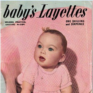 May include: Vintage magazine cover titled "baby's Layettes" featuring a baby in a pink outfit. The baby has blue eyes and is sitting on a pink surface. The text "Pretty Things for the First Year" is at the bottom.