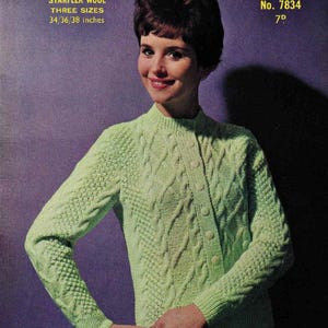 May include: A vintage advertisement for a knitted cardigan. The light green cardigan has a cable knit design and button closure. The text on the top left reads "DOUBLE KNITTING WOOL" and "THREE SIZES 34/36/38 inches". The Sirdar logo is in the top right.