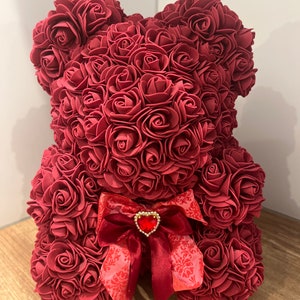 Könnte beinhalten: Ein burgunderfarbener Rosenbär mit einer roten Schleife und einem Juwelenherz-Akzent. Der Bär besteht aus künstlichen Rosen und ist ein romantisches Geschenk.