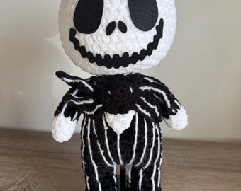 May include: A handmade crochet doll of Jack Skellington from The Nightmare Before Christmas. The doll has a white head with black eyes and a stitched smile. The body is black with white pinstripes, and the doll is standing upright.