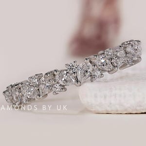 May include: A silver diamond ring featuring multiple clear gemstones. The ring showcases various diamond shapes, including pear and round cuts. The ring is presented on a white surface.