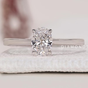 May include: A silver ring featuring a large oval-shaped diamond. The ring is displayed on a white surface with the text "DIAMONDS BY UK" visible in the background.