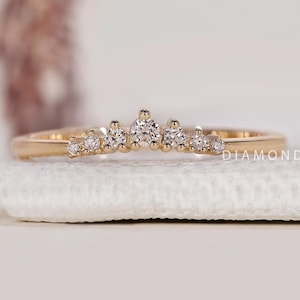 May include: A gold ring with a curved design, set with small diamonds. The ring is displayed on a white surface, highlighting its elegant and minimalist style. The ring is a piece of jewellery. The ring is a piece of jewellery.