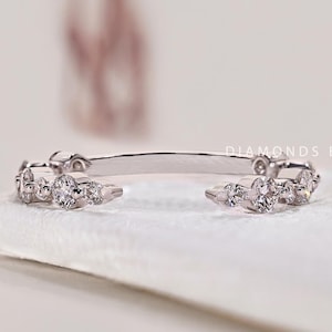 May include: A delicate silver ring with a row of small, round diamonds set in a curved band. The ring is on a white surface.