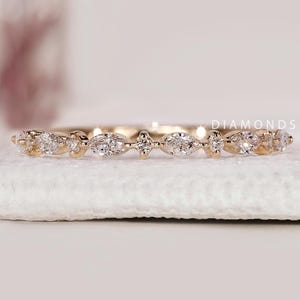 Peut inclure: Une bague en or ornée de petits diamants étincelants. Les diamants sont disposés en motifs répétés, avec des pierres rondes et en forme de marquise. La bague est présentée sur une surface blanche. Le texte "DIAMONDS BY UK" est visible.