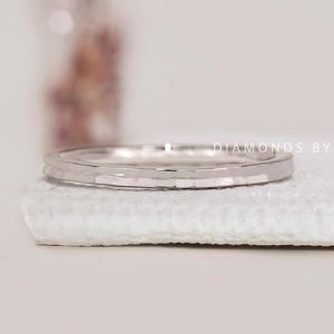 Könnte beinhalten: Ein silberner Ring mit gehammerter Textur, auf einer weißen Oberfläche. Der Ring hat ein schlichtes, elegantes Design. Die Worte "DIAMONDS BY UK" sind im Hintergrund sichtbar.