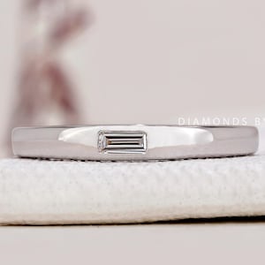 May include: A thin silver band with a single, rectangular-shaped diamond set in the centre.