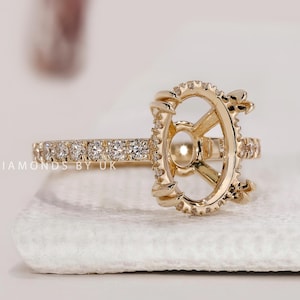 May include: A gold ring setting featuring an oval-shaped center mount with prongs, accented by a row of small round diamonds along the band and the perimeter of the setting. The text DIAMONDS BY UK is visible on the side of the ring band.
