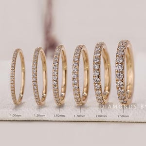 May include: Six gold rings with diamonds are displayed. The rings vary in width, from 1.00mm to 2.50mm, and are set with small, sparkling diamonds. The rings are arranged on a white surface, showcasing their design and craftsmanship. The rings are from Diamonds by UK.