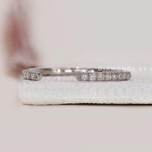 Peut inclure: Une bague ouverte en argent, sertie de petites pierres précieuses claires. La bague est présentée sur une surface blanche. Le texte "DIAMONDS BY UK" est visible en arrière-plan.