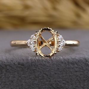 Könnte beinhalten: Ein goldener Ring mit einer leeren, ovalen Fassung in der Mitte, flankiert von drei kleinen, runden, klaren Steinen auf jeder Seite. Die Ringschiene ist aus glattem, poliertem Gold. Der Text "DIAMONDS BY UK" ist unter der Fassung zu sehen.