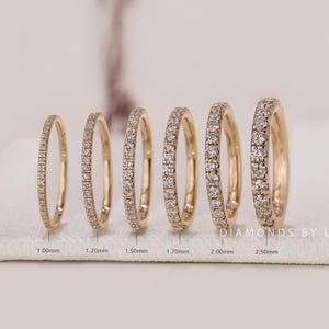 Peut inclure: Six alliances en or disposées en rangée, chacune sertie de petits diamants ronds. Les anneaux augmentent en largeur de 1,00 mm à 2,50 mm, avec des étiquettes indiquant la largeur spécifique de chaque bague. Le texte DIAMONDS BY UK est visible.