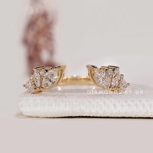 Peut inclure: Une bague dorée au design unique. Elle présente des pierres de taille marquise disposées en motif floral. La bague est posée sur une surface blanche. Le texte "DIAMONDS BY UK" est visible. C'est un bijou.