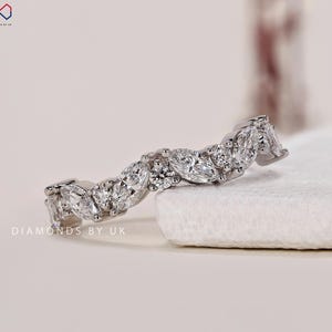 May include: A white gold ring with a series of marquise and round cut diamonds. The diamonds are set closely together, creating a continuous sparkle. The ring is displayed on a white surface, showcasing its brilliance.