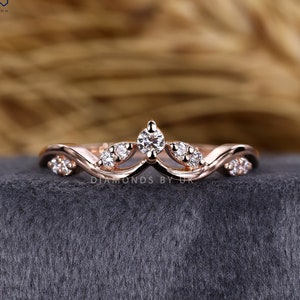 May include: Rose gold ring with a wave design, set with multiple small diamonds and a larger central diamond. The ring has a delicate, elegant appearance. The text "DIAMONDS BY UK" is visible on the ring.