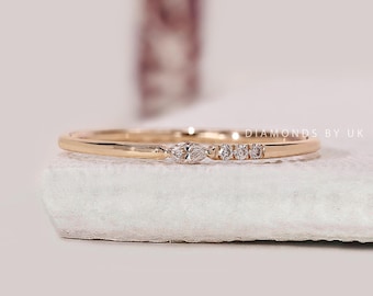 May include: A delicate gold ring featuring a marquise-cut diamond flanked by three smaller round diamonds. The ring is set on a thin, polished gold band. The ring is displayed on a white surface.