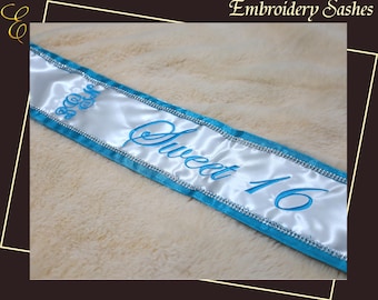 Op de afbeelding: Een witte satijnen sjerp met blauw geborduurde tekst "Sweet 16". De sjerp heeft een turquoise rand met zilveren afwerking. De woorden "Embroidery Sashes" staan bovenaan.