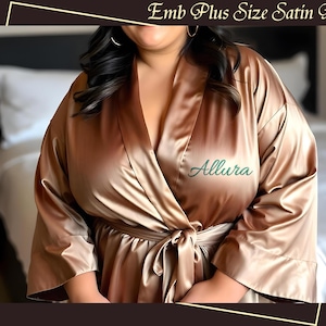 May include: A gold satin robe with a green embroidered name "Allura" on the left side. The robe has a tie belt and long sleeves.