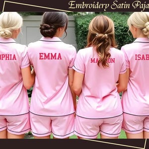 May include: Four pink satin pajamas with black trim and personalized embroidery. The names "Sophia", "Emma", "Madison", and "Isabelle" are embroidered in red on the front of each pajama top.