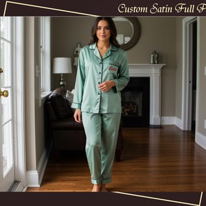 Peut inclure: Un ensemble de pyjama en satin vert menthe avec des bordures noires. Le haut à manches longues a une fermeture boutonnée et un petit détail brodé. Le pantalon assorti a une coupe décontractée. Le texte "Custom Satin Full Pajama" est en haut de l'image.
