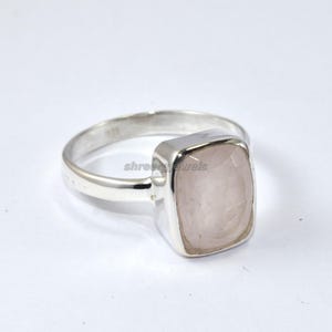 May include: A silver ring with a square, light pink gemstone. The gemstone is set in a square bezel and the band is smooth and polished. The ring is displayed on a white background. The text "shreejewels" is visible on the ring.