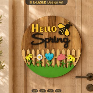 May include: A circular wooden door sign featuring the text Hello Spring in yellow and black lettering. The design includes a yellow and black bee, a light brown picket fence, and colorful flowers in yellow, white, blue, and pink on green grass.
