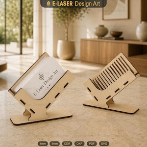 May include: Two light-colored wooden business card holders with a slotted design. One holder contains a white business card with the text E-Laser Design Art. The holders feature a flat base and an angled support structure with visible joinery.