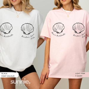 May include: A white t-shirt and a light pink t-shirt, each featuring two black line-art seashell graphics. Below the shells, the text reads "Olivia's Bachelorette" and "Barcelona, Spain 2026" in a black cursive font. Both shirts have short sleeves.
