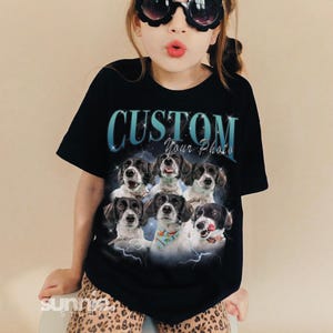 以下が含まれることがあります： 前面に「CUSTOM Your Photo」という文字が印刷された、ヴィンテージスタイルの複数の犬のグラフィックが描かれた黒いTシャツです。