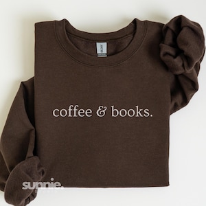 Op de afbeelding: Een donkerbruine sweatshirt met de tekst "coffee & books." in een lichte kleur. De sweatshirt heeft lange mouwen en een ronde hals. De merknaam "sunnie studio" staat linksonder.