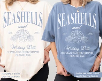 May include: A natural-colored t-shirt with light blue text and a blue t-shirt with white text. Both feature the words SEASHELLS and Wedding Bells, EST. 2026, and OLIVIA'S BACHELORETTE FRANCE 2026, along with a graphic illustration of three seashells.