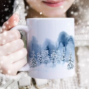 May include: White ceramic mug with a watercolor design of a snowy forest scene. The mug has a blue and white color scheme and features a variety of trees.
