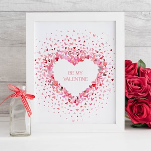 Puede incluir: Una impresi&oacute;n enmarcada en blanco con un coraz&oacute;n rosa hecho de corazones rosas m&aacute;s peque&ntilde;os. El texto "BE MY VALENTINE" est&aacute; dentro del coraz&oacute;n. La impresi&oacute;n est&aacute; sobre una superficie blanca con una botella de vidrio transparente y un ramo de rosas rojas.