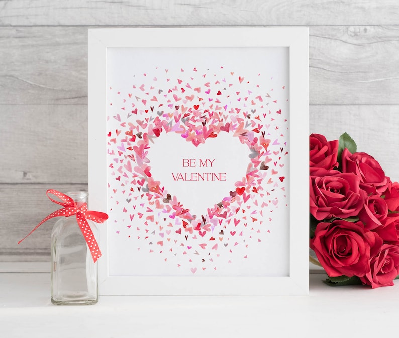 Puede incluir: Una impresi&oacute;n enmarcada en blanco con un coraz&oacute;n rosa hecho de corazones rosas m&aacute;s peque&ntilde;os. El texto "BE MY VALENTINE" est&aacute; dentro del coraz&oacute;n. La impresi&oacute;n est&aacute; sobre una superficie blanca con una botella de vidrio transparente y un ramo de rosas rojas.