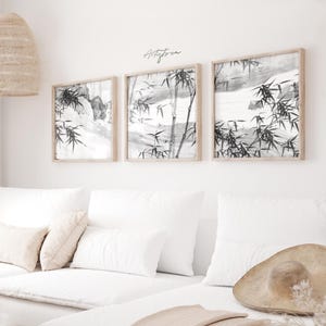 Peut inclure: Trois impressions d'art encadrées avec un motif de forêt de bambous en noir et blanc. Les impressions sont dans des cadres en bois clair et sont accrochées sur un mur blanc. Le texte "Artistica" est écrit au-dessus des impressions. Les impressions sont au-dessus d'un canapé blanc avec des coussins.