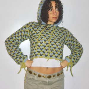 Può includere: Una felpa con cappuccio all'uncinetto a maniche lunghe con un motivo a chevron ripetuto in azzurro, verde oliva e nero. Il capo corto presenta un cappuccio con coulisse, maniche lunghe con dettagli a laccio sui polsini e una lavorazione traforata.