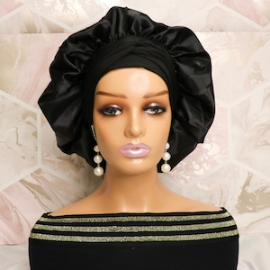 Puede incluir: Un gorro de dormir de satén negro con la parte superior fruncida. El gorro se lleva en un maniquí con una parte superior negra y ribete dorado.