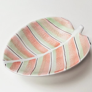 Puede incluir: Un plato de cerámica blanca con forma de hoja con un diseño de rayas rosas y verdes.