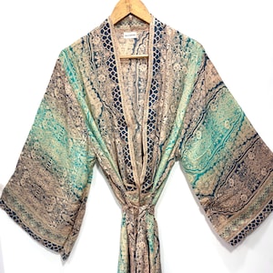 Könnte beinhalten: Langer, offen geschnittener Morgenmantel mit Paisley-Muster in Türkis, Beige und Marineblau. Der Morgenmantel ist aus leichtem Stoff gefertigt und hat weite Ärmel. Er hängt an einem Holzkleiderbügel.