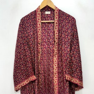 May include: A burgundy floral print kimono-style jacket with a gold and red border. The jacket is hanging on a wooden hanger against a white background. The floral pattern is a mix of red and gold.