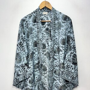 May include: A pale blue kimono with a black and grey floral design. The top is hanging on a wooden hanger. The sleeves are long and wide, and the fabric appears lightweight. The garment has a decorative border.