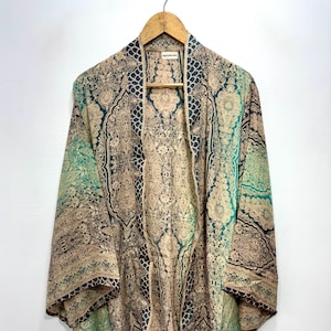 Może przedstawiać: Wzorzysta kurtka w stylu kimono w odcieniach beżu, turkusu i granatu wisi na drewnianym wieszaku. Kurtka z otwartym przodem ma skomplikowany wzór paisley. Rękawy są do trzech czwartych.